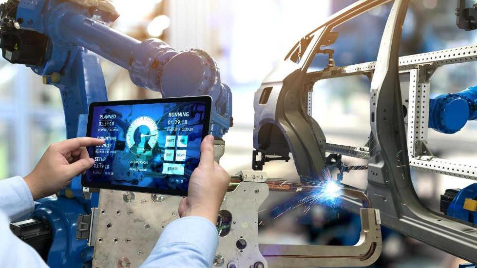 profesional de fábrica que utiliza un dispositivo electrónico portátil para interactuar con equipos de fábrica autónomos